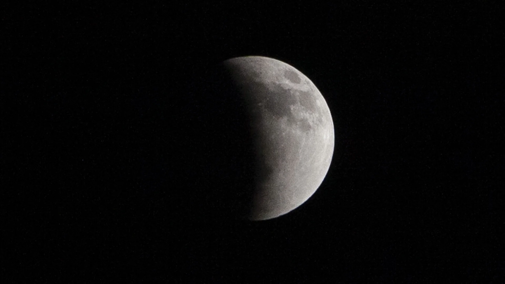 Uma lua cheia é fotografada em um céu negro, com sua metade esquerda imersa na sombra curva da Terra durante um eclipse lunar.