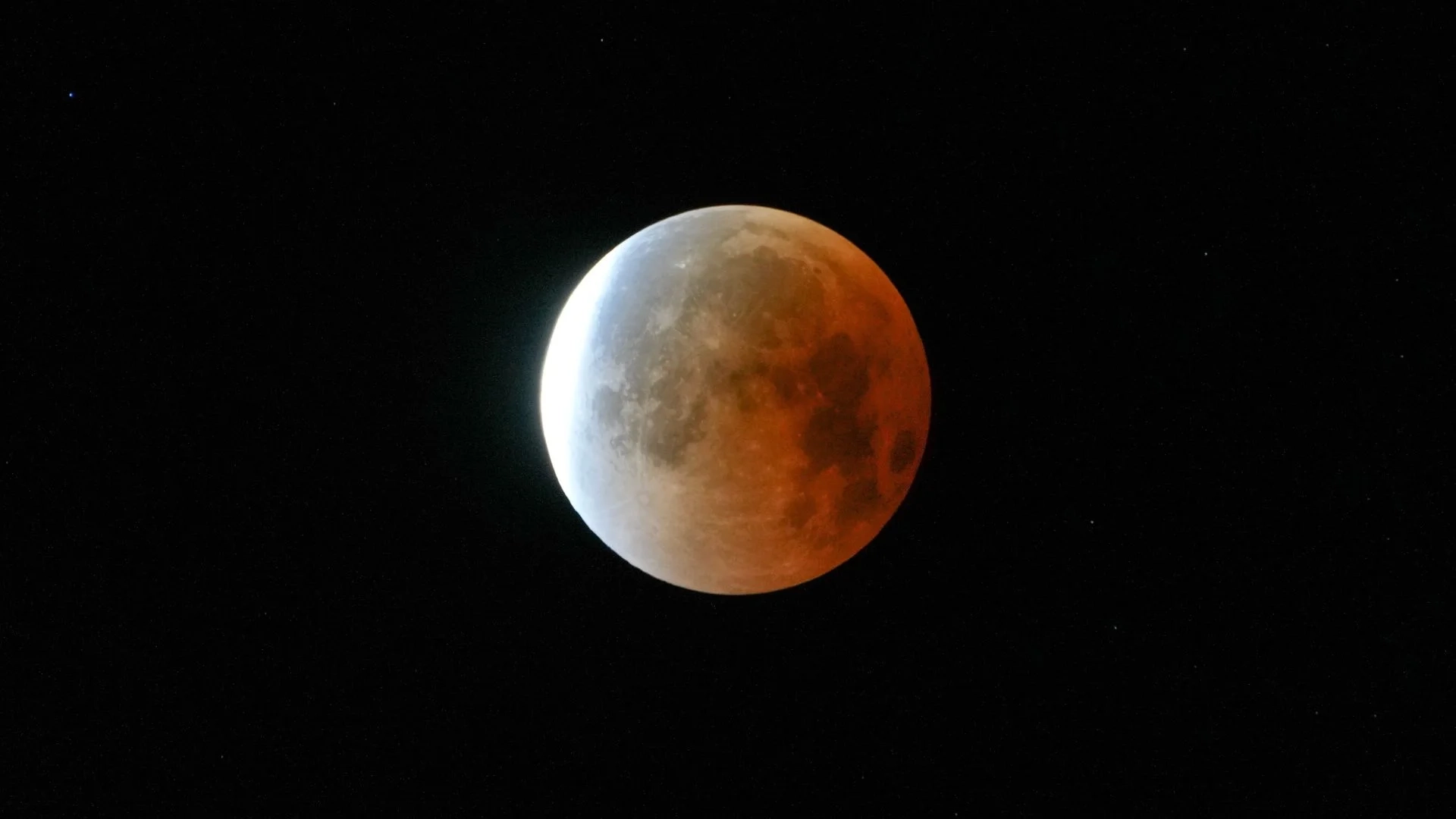 Durante um eclipse lunar, uma lua cheia pode ser vista no céu negro, cujo lado direito brilha em vermelho na sombra da Terra.