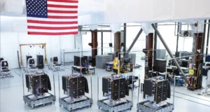 Novas sondas “perceptoras” privadas ficarão de olho nos satélites bem acima da Terra four cubical spacecraft sit inside a large white-walled clean room with an american flag in the background