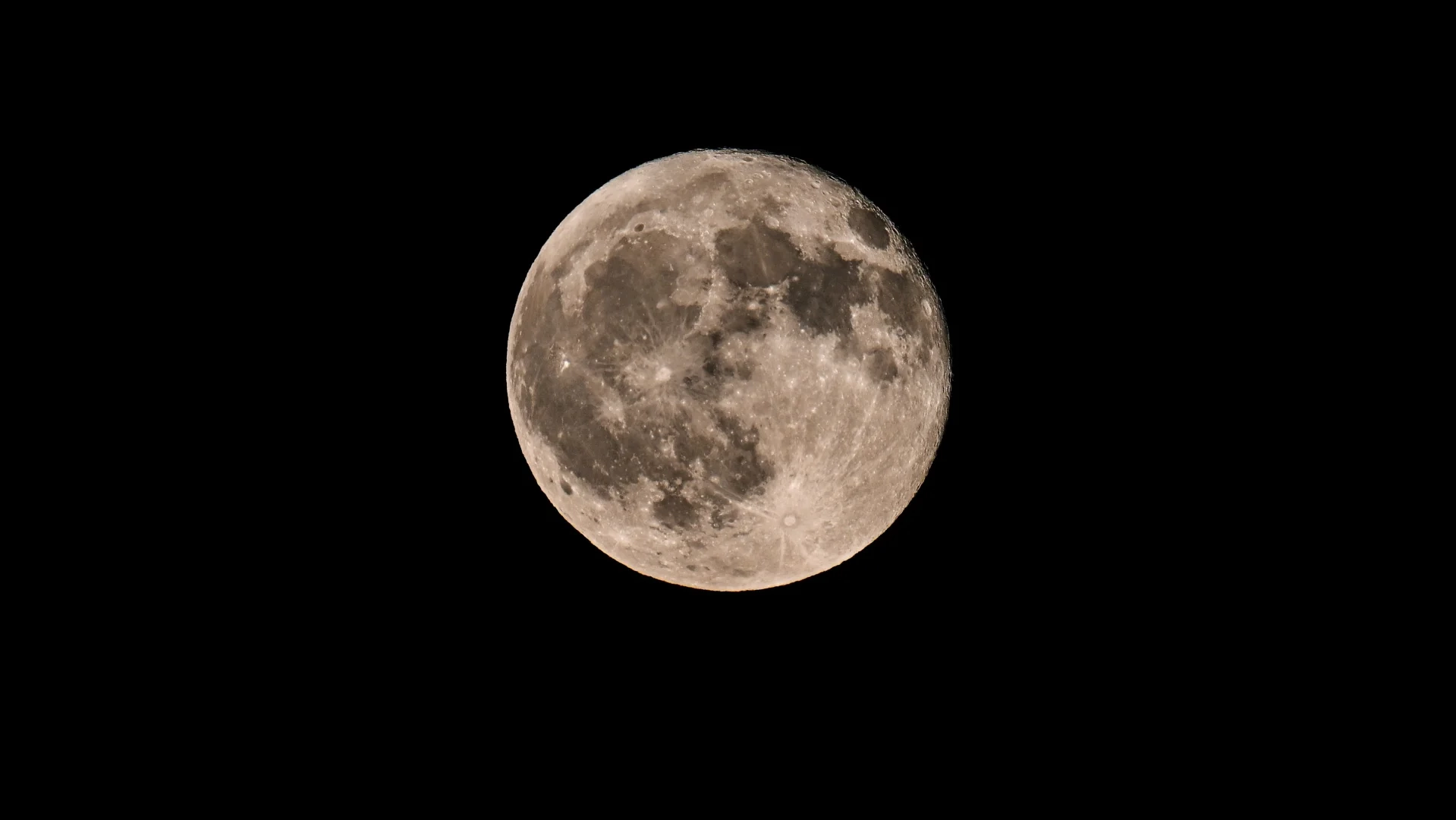 Uma lua cheia é fotografada em um céu noturno negro com mares lunares escuros e crateras em sua superfície.
