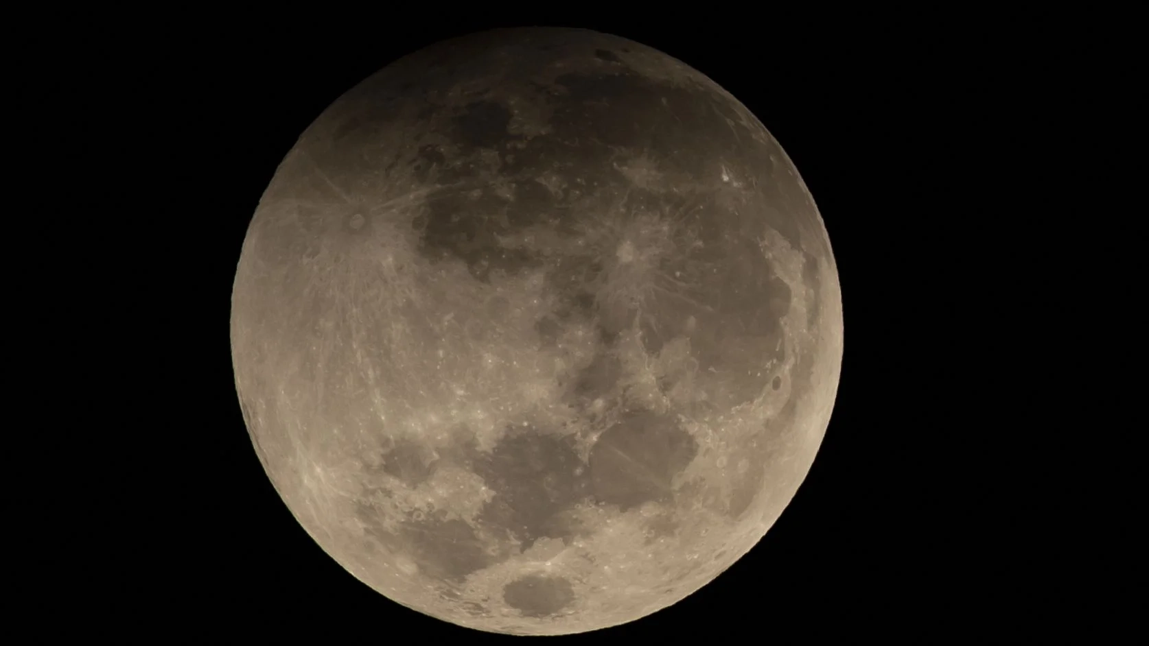 Uma lua cheia é vista em um céu negro com a borda superior sombreada durante um eclipse lunar parcial.