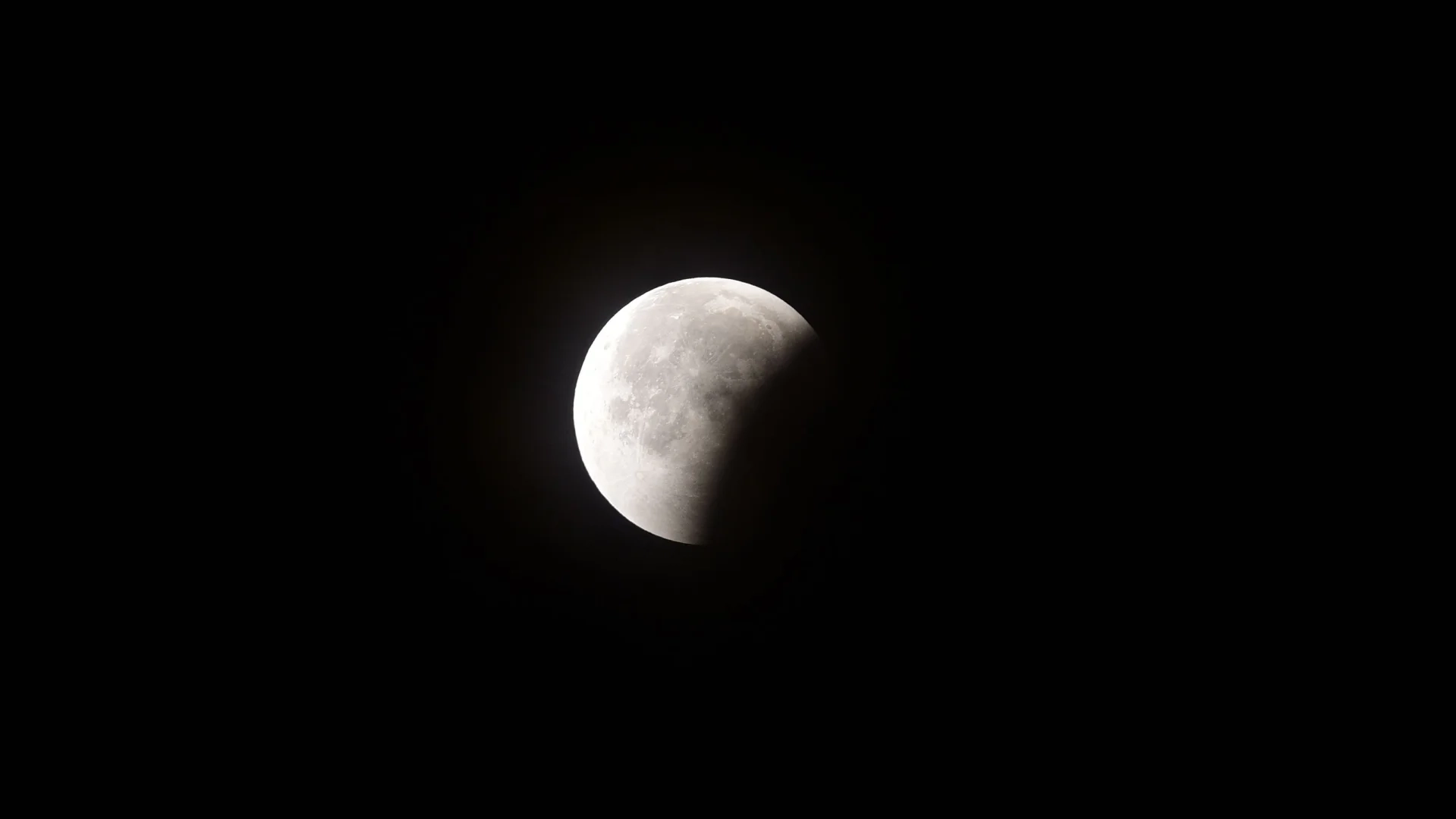 Uma lua cheia é fotografada em um céu negro durante um eclipse lunar, com sua parte inferior direita obscurecida pela sombra curva da Terra.